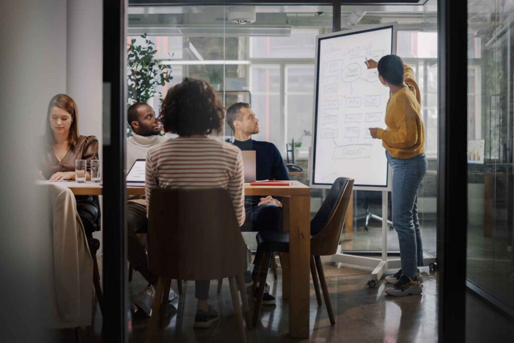 Marketing team collaborating during a strategy meeting with a presenter explaining campaign goals on a whiteboard.